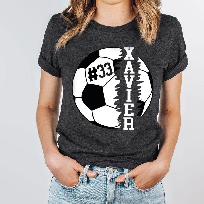 May include: A dark grey t-shirt featuring a white football graphic. The ball is split in half, with the word "XAVIER" written vertically on the right side and the number "#33" on the left side.