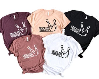 Pode incluir: Cinco camisetas de diferentes cores com um gráfico de pinos e bola de boliche e o texto "GRACE: CHARLOTTE".