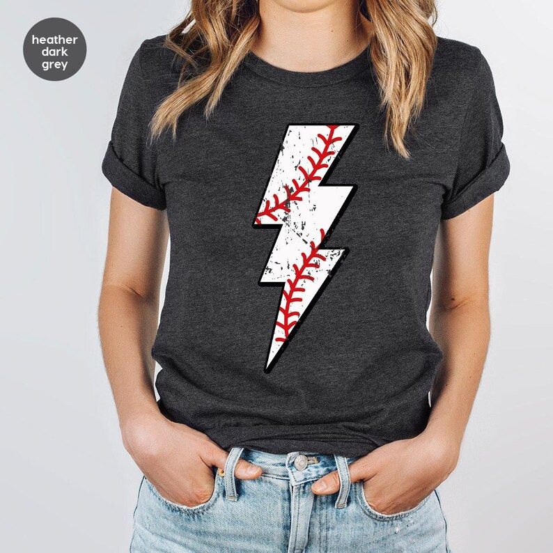 May include: Heather dark grey t-shirt with a white lightning bolt graphic. The lightning bolt is filled with a baseball pattern.