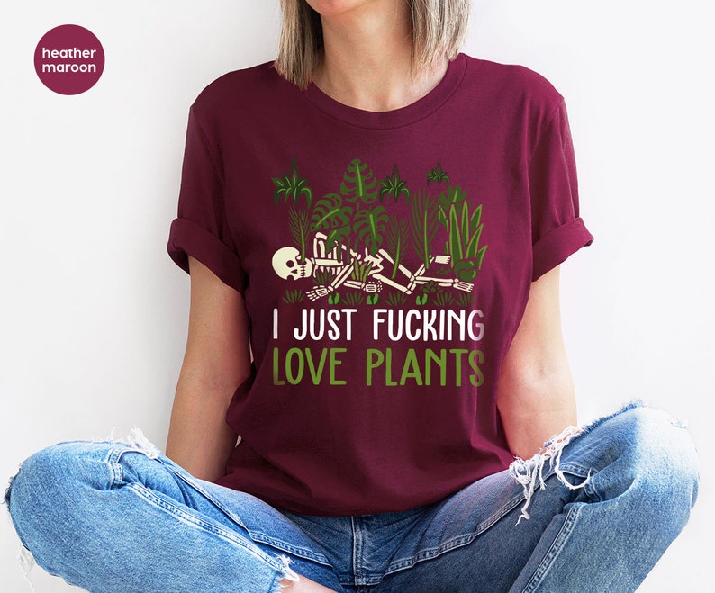 May include: A heather maroon t-shirt with a graphic of a skeleton lying in a bed of green plants. The text "I JUST FUCKING LOVE PLANTS" is printed in white below the graphic.