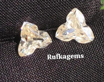 May include: Two clear, faceted gemstones with a unique, three-lobed shape. The gems are displayed on a black surface, with the text "Rufkagems" in white. The gems sparkle, reflecting light.