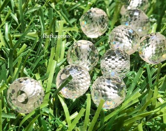 May include: Clear, faceted crystal spheres scattered on green grass. The spheres have a cut-glass appearance, reflecting light and creating a sparkling effect. The image is well-lit, highlighting the details of the crystal and the texture of the grass.