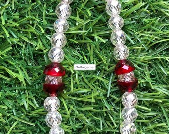 May include: A beaded necklace featuring alternating clear faceted crystal beads and deep red faceted glass beads arranged in a circular pattern. A small white rectangular tag with the black text Rufkegems is positioned in the center of the necklace.