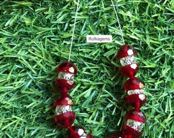 May include: A strand of faceted beads alternating between deep red and clear transparent glass, arranged in a U-shape. The beads are strung on a thin white cord, and a small white rectangular label with the text Rufkagems is visible.