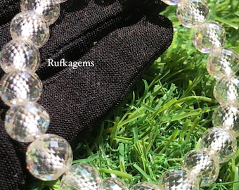 May include: A clear quartz beaded bracelet with faceted, spherical beads. The bracelet is displayed against a black background and green grass. The text "Rufkagems" is visible on the black background.