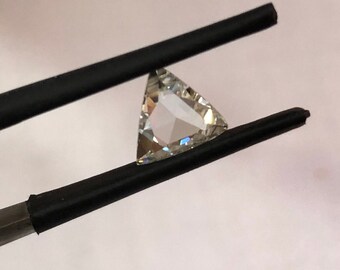 Puede incluir: Una piedra preciosa triangular transparente con facetas, sostenida por pinzas negras.