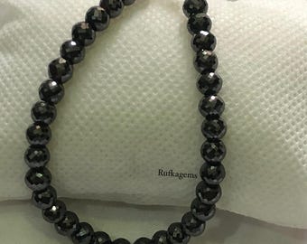 May include: A bracelet composed of round, faceted black beads with a metallic sheen. The beads are strung together and secured with a silver-toned lobster claw clasp. The text Rufkagem is printed in small black letters near the center of the beads.