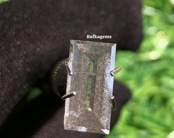 May include: A rectangular, clear gemstone ring with a silver setting. The gemstone has a subtle green hue and is held in place by four silver prongs. The ring is displayed against a dark background with the text "Rufkagems".