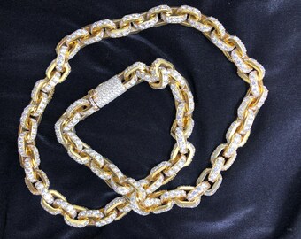 May include: A gold-toned chain necklace and bracelet set. The chain links are encrusted with small, clear gemstones. The clasp on the bracelet is also covered in gemstones. The jewelry is displayed on a black surface.