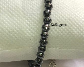 May include: A bracelet featuring a single strand of small, dark gray, faceted spherical beads. The jewelry piece includes a silver-toned metal chain extender and a lobster claw clasp. The text "Rufkagem" is visible near the center of the beads.