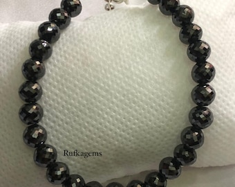 May include: A bracelet composed of round, faceted black beads arranged in a circular pattern. The jewelry features a silver-toned metal lobster claw clasp and an adjustable chain link extension. The text Rufkagems is printed near the beads.