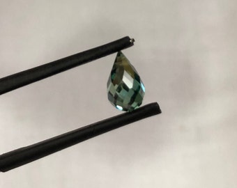 May include: A teardrop-shaped green gemstone with facets, held by tweezers.