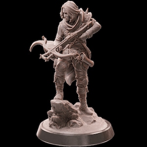 May include: A detailed miniature figurine of a person holding a crossbow, standing on a rocky base. The figurine is made of a light brown material and is painted in a realistic style.