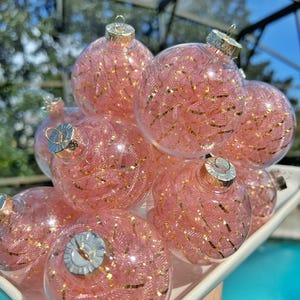 May include: A set of pink and gold Christmas ornaments. The ornaments are made of clear glass and filled with pink and gold glitter. They are perfect for adding a touch of sparkle to your Christmas tree.