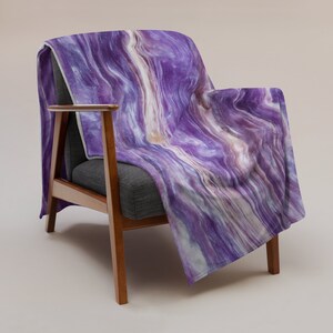 May include: A purple and white patterned fleece throw blanket draped over a wooden armchair.
