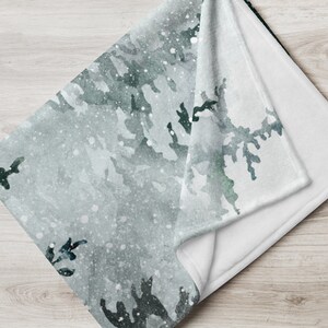 以下が含まれることがあります： 緑とグレーの木々を水彩で描いた、雪景色を背景にした、柔らかく白いフリースの毛布です。