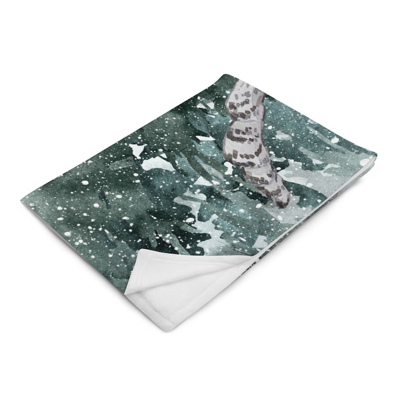 以下が含まれることがあります： 雪の降る森の風景が水彩画で描かれた、柔らかくふわふわの毛布。緑と白のカラーリングで、雪の結晶がさりげなく模様になっています。