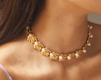 May include: A gold necklace with a delicate chain and leaf-shaped pendants accented with small white pearls.