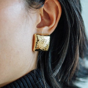 May include: A pair of gold square earrings with a hammered texture.