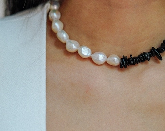 Puede incluir: Un collar de perlas blancas con cuentas negras en un lado. El collar lo lleva una persona con una camisa blanca.