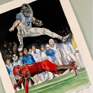 May include: Watercolor painting of a football game with a player in a blue and white uniform jumping over a player in a red uniform. The background shows a crowd of people in the stands. The painting is signed "Hand Drawn 2023" and includes the artist's social media handle "@hclaytonart".