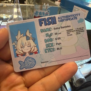 May include: A blue and white authenticity certificate featuring the name "Saba Sameko" and the word "FISH" in large letters. The certificate includes details such as height (35 cm), date of birth, and eye color. A cartoon fish graphic is also present.