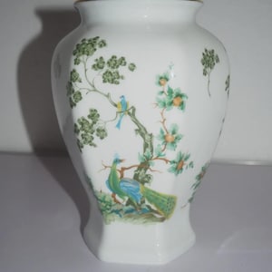 Peut inclure: Vase en céramique blanche avec un bord doré et une base hexagonale. Le vase présente un motif peint à la main d'un paon, d'oiseaux et de branches fleuries dans des tons de vert, de bleu et d'orange. Une pièce décorative pour la décoration intérieure.