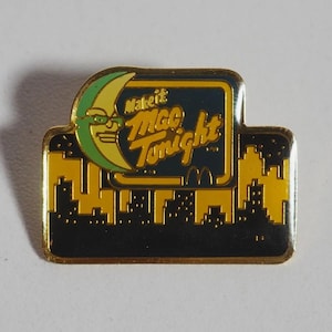 Puede incluir: Un pin de metal esmaltado en tono dorado con una luna creciente amarilla que lleva gafas de sol verdes. El texto "Make it Mac Tonight" aparece en letra cursiva amarilla. Debajo, una silueta urbana amarilla sobre un fondo negro.