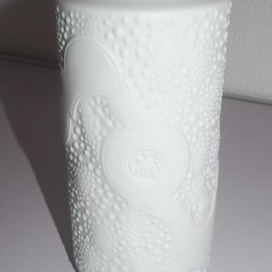 Puede incluir: Jarrón de cerámica blanca con forma cilíndrica. El jarrón presenta una superficie texturizada de pequeños puntos en relieve y un diseño en relieve decorativo. La abertura superior es lisa y redonda.