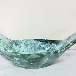 Op de afbeelding: Een handgemaakte, vogelvormige kom met een teal en groene gemarmerde afwerking. De keramische kom heeft een lange, gebogen body met een kop en staart, perfect voor decoratief gebruik of serveren. De kom is ongeveer 40 cm lang.