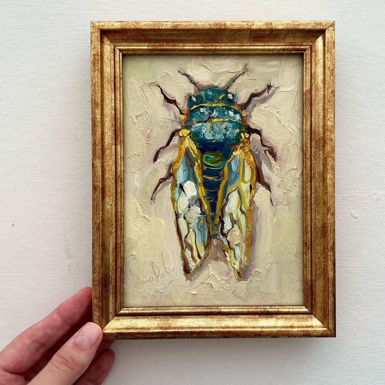 May include: Oil painting of a cicada in a gold frame. The insect is depicted with a teal and yellow body and wings, set against a cream-colored background. The frame has a detailed, ornate design.
