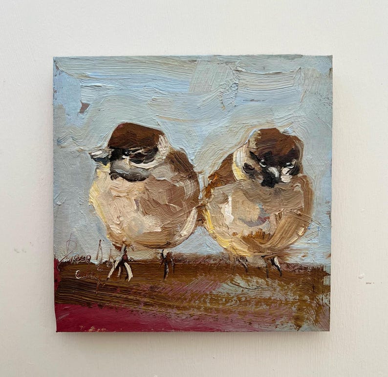 Puede incluir: Una pintura al &oacute;leo sobre lienzo cuadrado que muestra dos peque&ntilde;os p&aacute;jaros marrones y blancos posados uno al lado del otro. Los p&aacute;jaros tienen cabezas de color marr&oacute;n oscuro y cuerpos marrones claros, sobre un fondo azul claro texturizado.