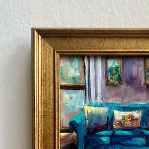 May include: A framed oil painting depicts a teal sofa with decorative pillows. The artwork features a gold-colored frame and a view of a window with curtains. The painting's style is impressionistic, with visible brushstrokes and a focus on color and light.