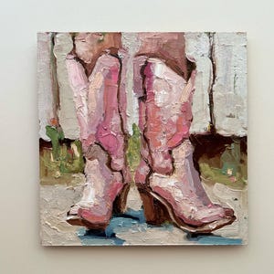 Puede incluir: Pintura al &oacute;leo de dos botas de vaquero rosas con tacones marrones. Las botas est&aacute;n pintadas con pinceladas gruesas, lo que les da una apariencia texturizada. El fondo presenta toques de verde y blanco, lo que sugiere un entorno al aire libre.