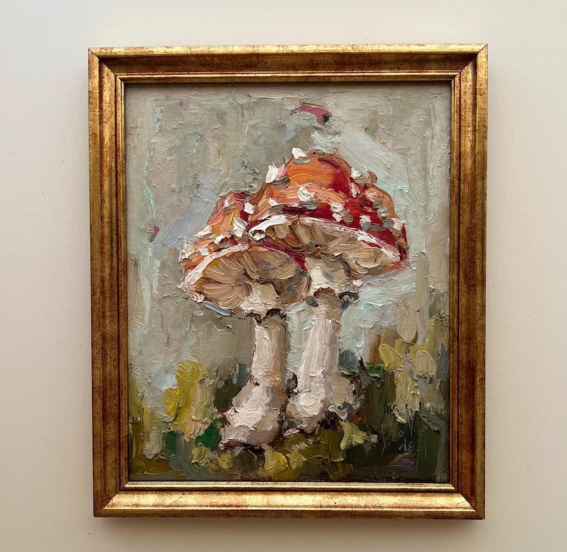 May include: An oil painting of two mushrooms with red caps and white spots, rendered with thick, visible brushstrokes. The mushrooms have pale stems and are set against a muted, textured background. The artwork is enclosed in a gold frame.