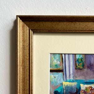May include: A framed painting with a gold-colored ornate frame. The painting depicts an interior scene with a sofa, curtains, and other decorative elements. The artwork is in a colorful, impressionistic style.