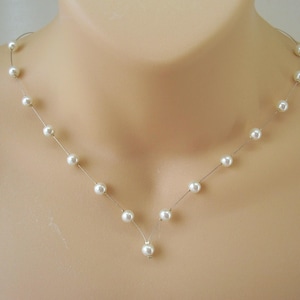 May include: A delicate necklace featuring a series of white, round pearls strung on a thin, nearly invisible wire. The pearls are evenly spaced, creating a graceful, V-shaped design. The necklace is displayed on a neutral background, highlighting the jewelry's simplicity.