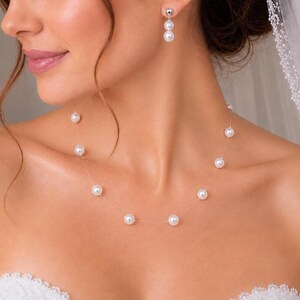 May include: A necklace featuring evenly spaced white pearls on a thin, transparent cord, paired with matching drop earrings that each consist of two white pearls stacked vertically on a silver-toned metal post and backing.
