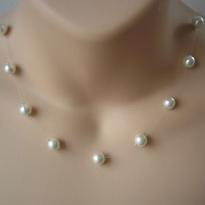 May include: A delicate pearl necklace with a clear string and white pearls. The necklace is on a mannequin's neck.