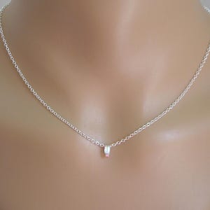 Könnte beinhalten: Eine zarte Silberkette mit einem kleinen Anhänger. Der Anhänger hat einen rosa Akzent. Die Halskette wird am Hals und an der Brust einer Person gezeigt.