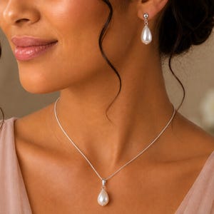 May include: A silver necklace featuring a single white teardrop-shaped pearl pendant on a delicate chain, paired with matching drop earrings. Each earring consists of a small silver stud connected to a white teardrop-shaped pearl pendant.
