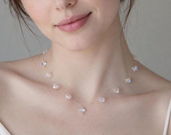 May include: A delicate necklace featuring a thin, transparent nylon cord adorned with multiple small, faceted, iridescent crystal beads that catch the light with subtle blue and pink reflections, spaced evenly along the length of the cord.