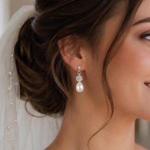 May include: Elegant drop earrings featuring a sparkling, round, clear crystal accent above a large, pear-shaped, white pearl. The earrings are silver-toned and dangle gracefully. Perfect for weddings or special occasions.