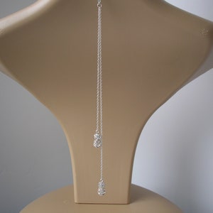 May include: A silver necklace with a fine chain. The necklace has two clusters of small, sparkling crystals, one near the middle and one at the end of the chain. The necklace is displayed on a mannequin.