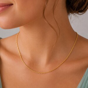 May include: A delicate gold chain necklace featuring a classic cable link design. The necklace rests against the neck, showcasing a polished metallic finish and a simple, uniform structure that connects seamlessly around the collarbone area.