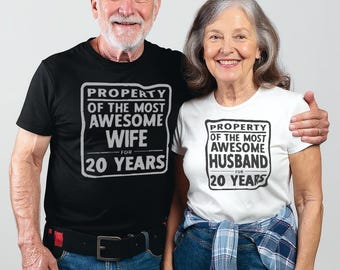 May include: A couple wearing matching t-shirts. The black shirt reads "PROPERTY OF THE MOST AWESOME WIFE FOR 20 YEARS." The white shirt says "PROPERTY OF THE MOST AWESOME HUSBAND FOR 20 YEARS." Both shirts have a rectangular design.