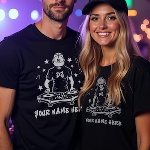 May include: Two black t-shirts featuring a white graphic of a DJ at a turntable with the text "DJ" and "YOUR NAME HERE". Both shirts are worn with plain black baseball caps. The graphic includes stars and musical notes surrounding the DJ figure.