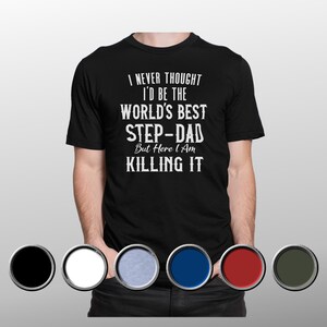 Può includere: T-shirt nero con testo bianco: "I NEVER THOUGHT I'D BE THE WORLD'S BEST STEP-DAD But Here I Am KILLING IT." La maglietta ha un girocollo e maniche corte. L'immagine mostra anche campioni di colore.