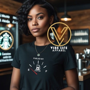 May include: Black t-shirt with a white graphic of a gas gauge with the text "Fueled by Coffee". The gauge is full and the needle points to the "F" on the gauge. The text "Vibe Life Apparel" is in a gold circle on the right side of the shirt.
