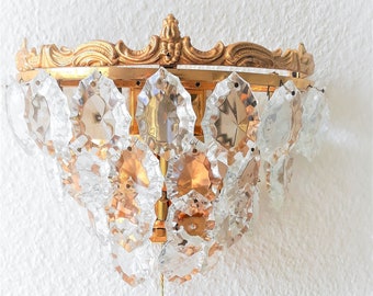 Può includere: Un'applique da parete dorata con un design a lampadario di cristallo. L'applique ha una catenella per accendere e spegnere la luce.